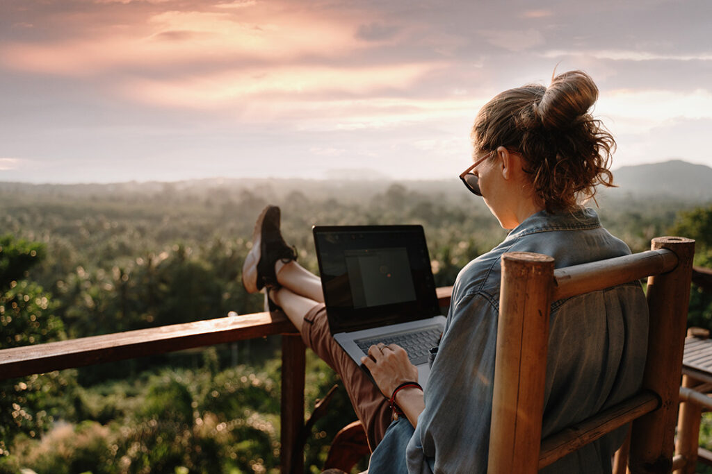 Kvinna sitter på en balkong i solnedgång och arbetar på en laptop